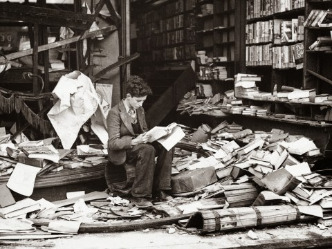 Young boy reading book in a ruined bookshop in London devastated by an air raid - 1940